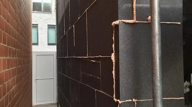 Smalle doorgang tussen twee panden met rechtergevel bekleed met zwarte isolatieplaten en zichtbare kitnaden.